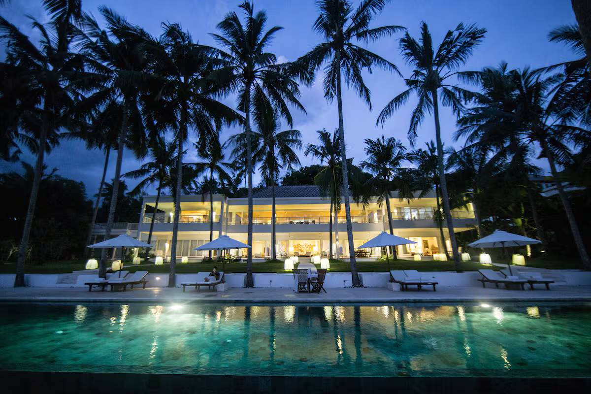 Beachfront villa and pool illuminated at dusk beneath palm trees